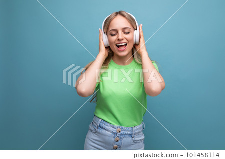 adorable blond girl in casual outfit dancing to music in big white headphones on a blue background adorable blond girl in casual outfit dancing to music in big white headphones on a blue background 101458114
