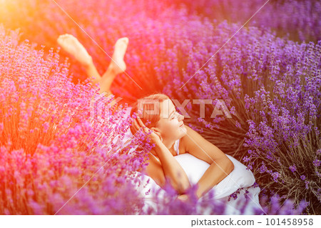 A middle-aged woman lies in a lavender field and enjoys aromathe 101458958