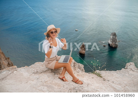 Freelance women sea working on the computer. Good looking middle aged woman typing on a laptop keyboard outdoors with a beautiful sea view. The concept of remote work. Freelance women sea working on the computer. Good looking middle aged woman typing on a laptop keyboard outdoors with a beautiful sea view. The concept of remote work. 101458960