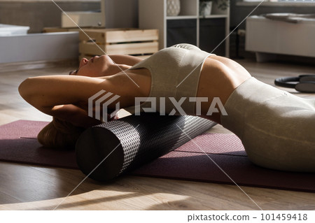 Fitness concept. Close up of woman relaxing after workout on the exercising yoga mat. Portrait of Active Woman Using Foam Roller for back and spine exercise Fitness concept. Close up of woman relaxing after workout on the exercising yoga mat. Portrait of Active Woman Using Foam Roller for back and spine exercise 101459418