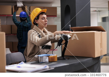 Retail storehouse manager packing cardboard box at counter desk and closing package. Caucasian warehouse worker wearing safety helmet preparing customer parcel for delivery 101460778