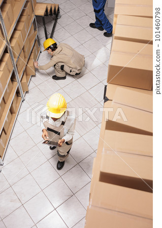 Delivery warehouse workers packing cardboard box and searching parcel using checklist on digital tablet. Industrial storehouse assistants preparing customer order for transportation Delivery warehouse workers packing cardboard box and searching parcel using checklist on digital tablet. Industrial storehouse assistants preparing customer order for transportation 101460798