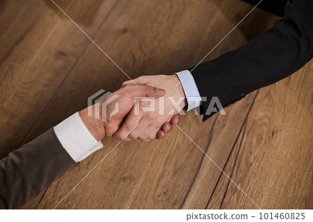 Closeup of hands of two young and successful male business people shaking hands over wooden table Closeup of hands of two young and successful male business people shaking hands over wooden table 101460825