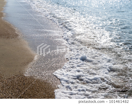 The white waves crashing on the sandy beach reflect the sunlight and sparkle. 101461482