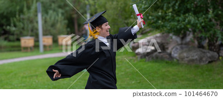 Caucasian woman in graduate gown dancing for joy outdoors.  101464670