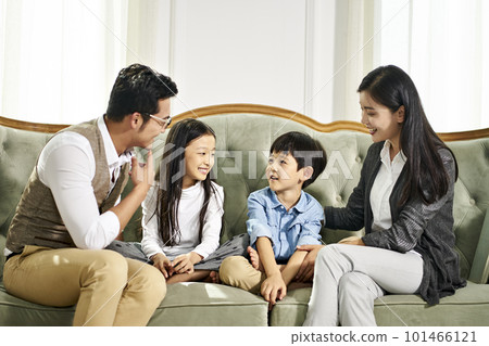 young asian father and mother and two children sitting on couch chatting in family living room at home 101466121
