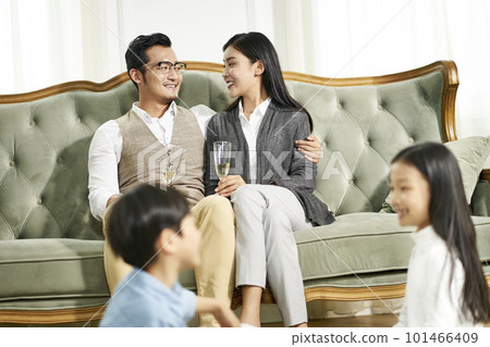 asian brother and sister sitting on carpet playing while parents chatting in background, focus on parents 101466409