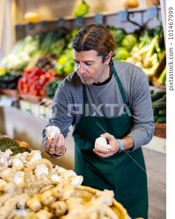 Male seller holding garlic standing in fruit and vegetable section of supermarket Male seller holding garlic standing in fruit and vegetable section of supermarket 101467999