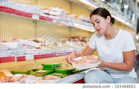 Woman comparing packaged mutton in animal products section of store 101468001