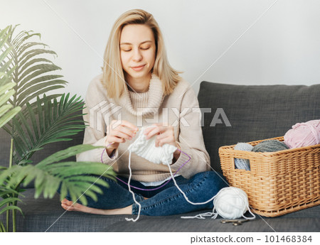 Young woman knitting warm scarf indoors 101468384