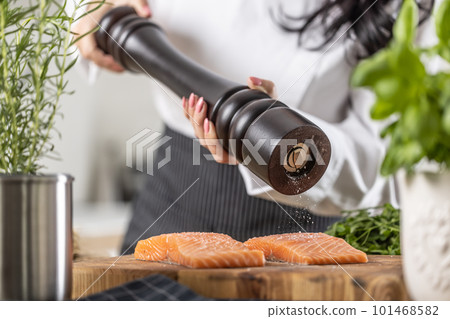 Classic wooden black pepper grinder used by a chef to season fillets of salmon Classic wooden black pepper grinder used by a chef to season fillets of salmon 101468582