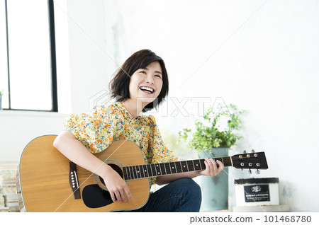 Smiling young woman playing guitar 101468780