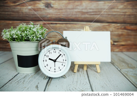 Empty card mockup with artificial plant and white alarm clock on wooden background Empty card mockup with artificial plant and white alarm clock on wooden background 101469004