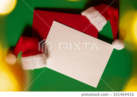 Santa hat with empty paper card note envelope on green background. Copy space for your text. Mock up for advertisement. Holiday Christmas composition Santa hat with empty paper card note envelope on green background. Copy space for your text. Mock up for advertisement. Holiday Christmas composition 101469428