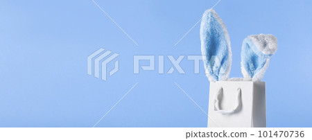 Wide banner on a blue background. The concept of online shopping for Easter, purchases and sale for the holiday. Gift bag with bunny ears and Easter eggs 101470736
