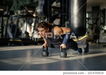 Young sportsman doing push-up exercise with kettlebell during training at gym Young sportsman doing push-up exercise with kettlebell during training at gym 101470919