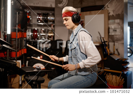 Hipster woman musician wearing headphones playing drum set at music shop 101471032