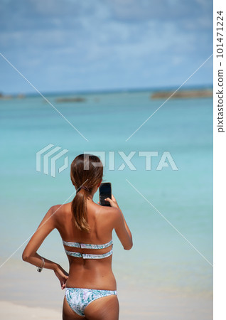 A young woman in a swimsuit using a smartphone at the beach 101471224