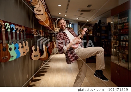 Overjoyed funny guitarist playing ukulele guitar at musical shop store Overjoyed funny guitarist playing ukulele guitar at musical shop store 101471229