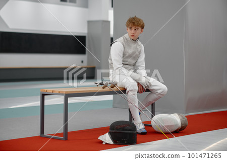 Tired young fencer in special costume sitting on bench and looking aside 101471265