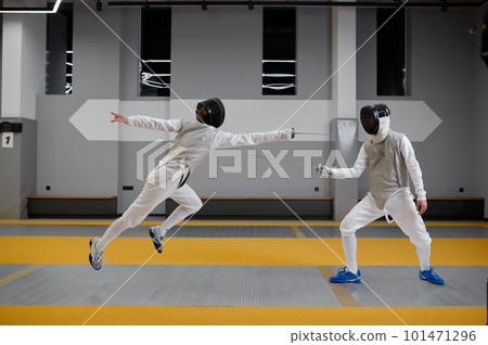 Athletes in uniforms and protective helmet mask fighting duel with rapiers Athletes in uniforms and protective helmet mask fighting duel with rapiers 101471296