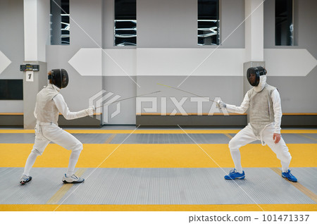 Two swordsmen wearing uniform fighting duel during training in sport gym room 101471337