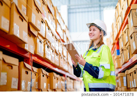 Pretty young warehouse worker woman hold tablet and look to product boxes on shelves 101471878