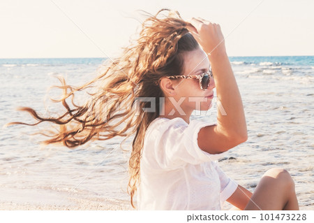 A young woman in sunglasses holds a hand to her hair fluttering 101473228