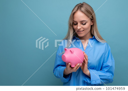 attractive blond girl holding a piggy bank on a blue isolated background attractive blond girl holding a piggy bank on a blue isolated background 101474959
