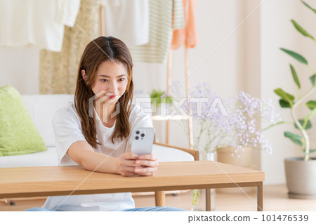Smiling woman looking at her smartphone in the living room Smiling woman looking at her smartphone in the living room 101476539