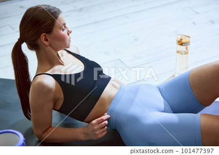 Young sportive girl in comfortable sportswear lying on fitness mat, resting after training session indoors 101477397
