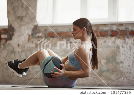 Athletic young woman with sportive, fit, strong body training with fitness ball, doing press exercises on mat indoors on daytime 101477529