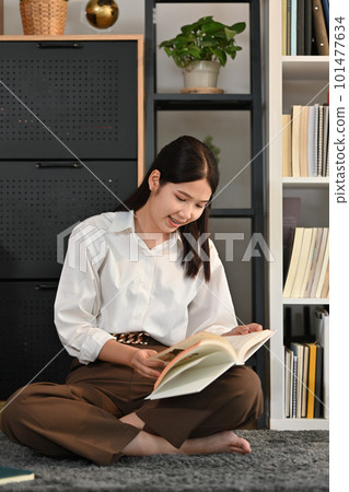 Beautiful young woman sitting floor in living room and reading a book, spending leisure weekend time at home 101477634