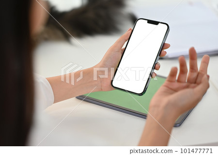 Close up view of woman using smartphone in front of laptop at office desk. White empty screen for app or web site design 101477771