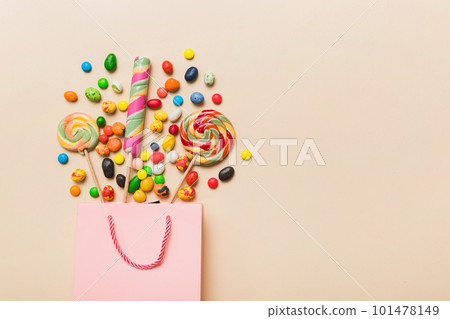 shopping paper gift bag in corner full of assorted traditional candies falling out on colored background with copy space. Happy Holidays sale concept shopping paper gift bag in corner full of assorted traditional candies falling out on colored background with copy space. Happy Holidays sale concept 101478149