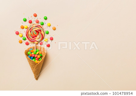 waffle cone full of assorted traditional candies falling out on colored background with copy space. Happy Holidays sale concept waffle cone full of assorted traditional candies falling out on colored background with copy space. Happy Holidays sale concept 101478954