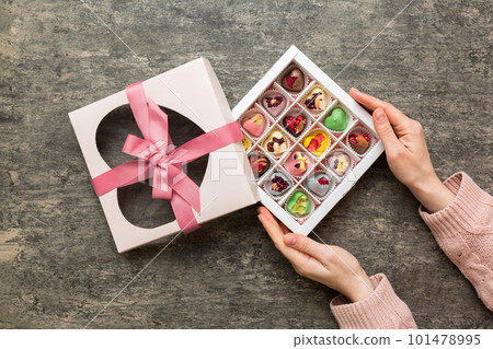 Female hands with delicious candies in box on color background Female hands with delicious candies in box on color background 101478995