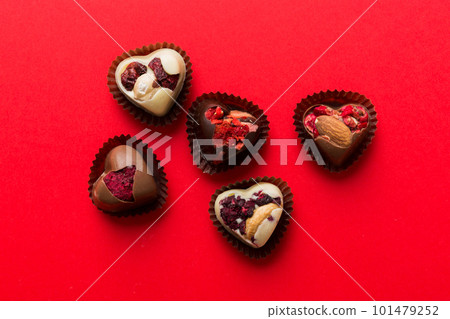 chocolate sweets in the form of a heart with fruits and nuts on a colored background. top view with space for text, holiday concept chocolate sweets in the form of a heart with fruits and nuts on a colored background. top view with space for text, holiday concept 101479252