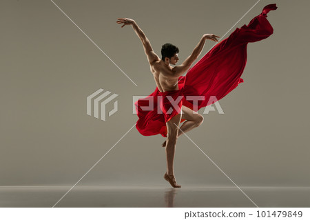 Young, handsome, muscular man dancing with red silk fabric against grey studio background. Modern ballet performance. 101479849