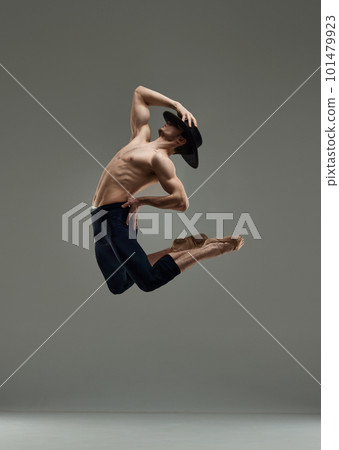 Handsome young man with muscular body dancing in hat and trousers, making creative performance against grey studio background Handsome young man with muscular body dancing in hat and trousers, making creative performance against grey studio background 101479923