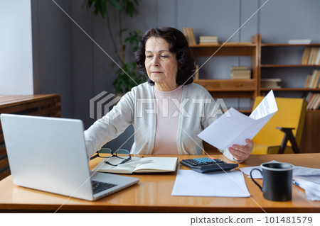 Middle aged senior woman sit with laptop and paper document. Pensive older mature lady reading paper bill pay online at home managing bank finances calculating taxes planning loan debt pension payment Middle aged senior woman sit with laptop and paper document. Pensive older mature lady reading paper bill pay online at home managing bank finances calculating taxes planning loan debt pension payment 101481579