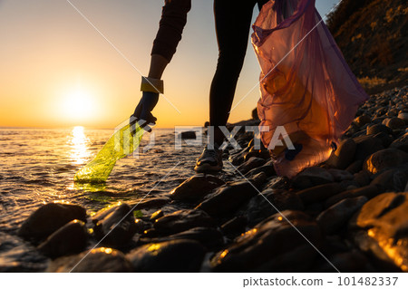 Earth day. A volunteer take a plastic bottle by the sea or river holding a plastic trash bag. Concept of coastal cleanup 101482337