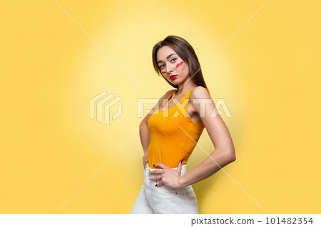 Feminism, girl power, and the concept of equal rights and independence for women. Caucasian young woman with makeup in an orange t-shirt posing in profile. Yellow background. Isolate. Copy space Feminism, girl power, and the concept of equal rights and independence for women. Caucasian young woman with makeup in an orange t-shirt posing in profile. Yellow background. Isolate. Copy space 101482354