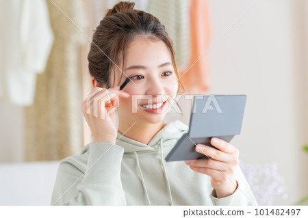 Young woman applying makeup in the living room Young woman applying makeup in the living room 101482497