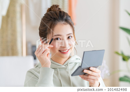 Young woman applying makeup in the living room 101482498