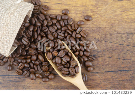 The Fresh roasted arabica coffee beans in a wooden spoon and scattered coffee beans on a wooden table 101483229