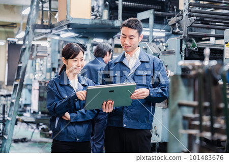 Staff discussing at the factory while looking at a tablet Staff discussing at the factory while looking at a tablet 101483676