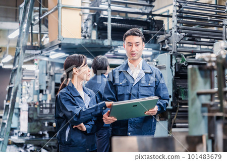Staff discussing at the factory while looking at a tablet Staff discussing at the factory while looking at a tablet 101483679