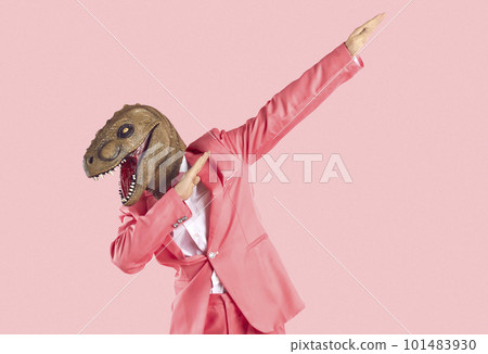 Cheerful young man in dinosaur rubber mask makes dab dance gesture isolated on pink background. 101483930
