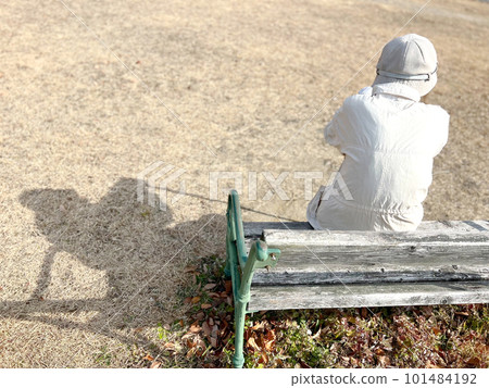 Elderly woman and shadow sitting on a bench outdoors Elderly woman and shadow sitting on a bench outdoors 101484192